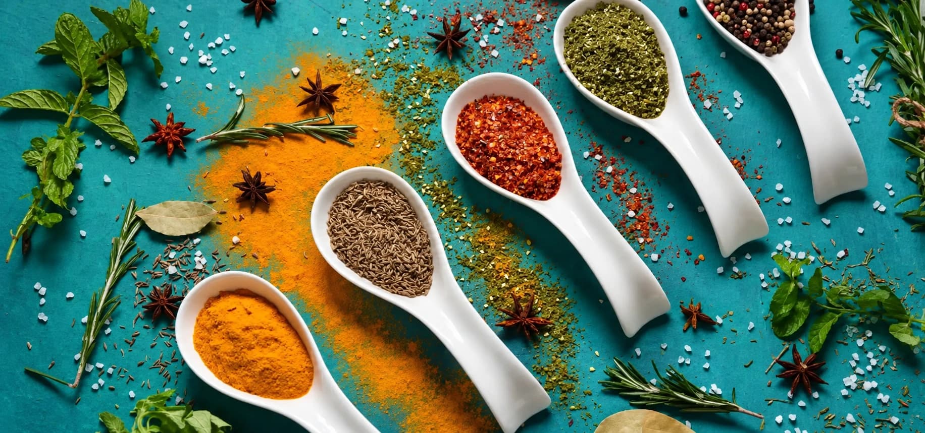 Assorted Indian spices in white ceramic spoons on a teal tabletop